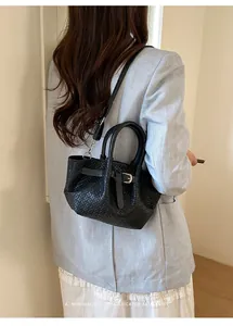 Woven leather bucket bag with top handle and strap shown on a model in a minimal setting