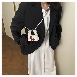 Mini white crossbody bag featuring black polka dots and a red horse applique on model