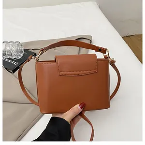 Detail of a brown PU leather bucket bag with a wide handle and gold hardware on a desk