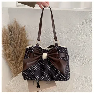 Detail of polka dot tote bag featuring a large brown leather bow and wavy lace trim