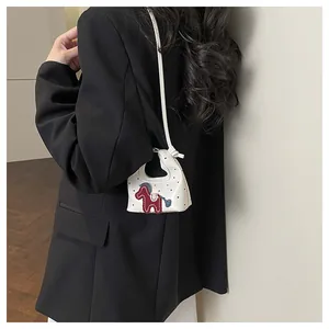 Detail of white polka dot mini bag with red horse charm and slender crossbody strap