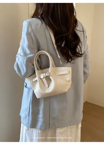 Detail of cream woven leather bucket bag with retro buckle and slim crossbody strap
