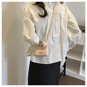 Detailed back view of a mini beige patent leather fashion handbag worn by a model