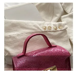 Close-up of rose red snake-embossed leather tote bag featuring a gold metal buckle and handle