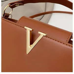 Close-up of brown leather bag featuring a polished gold V-shaped metal buckle and stitching