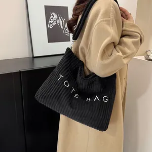 Large black corduroy tote bag with TOTE BAG embroidery shown from a model side view