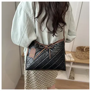 Detail of a black quilted tote bag with brown bow detail and slim shoulder strap