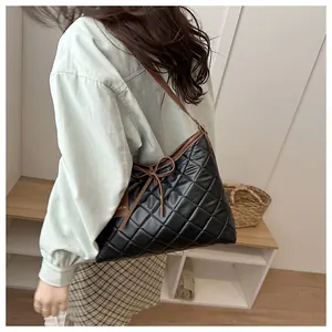 Detail of black quilted tote bag with bow accent and brown strap on model