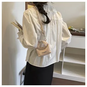 Detailed shot of a mini beige handbag with black FASHION text and thin shoulder strap