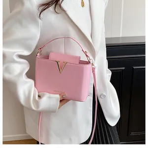 Detail showing pink leather handbag with gold V-shaped metal logo and fashion text