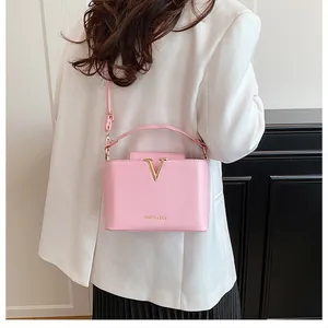 Detail view of pink leather crossbody bucket bag with golden V logo on white blazer