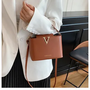 Detail of caramel brown leather bucket bag with gold V buckle on model in white blazer