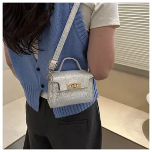 Detail of silver metallic textured mini crossbody bag with golden rotary lock and top handle