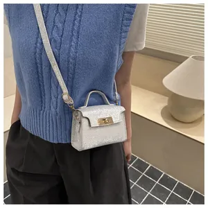 Detail of a silver glitter mini crossbody bag with gold turn-lock on a model