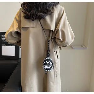 Close-up of zebra pattern mini bag with adjustable lanyard worn over a trench coat