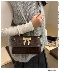 Detail of dark brown croc-pattern shoulder bag with a large golden butterfly metal buckle