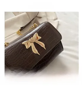 Detail of crocodile pattern small square bag with golden bow buckle on white fabric
