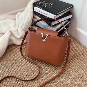 Minimalist brown bucket bag with gold V hardware and adjustable shoulder strap