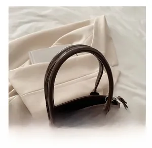 Detail of a shiny dark brown patent leather handbag with dual handles and a metal zipper