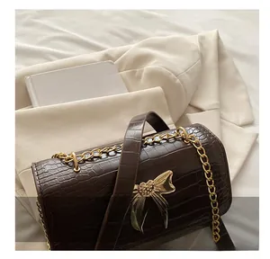 Detail of dark brown crocodile pattern bag with golden heart bow buckle and chain