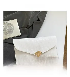 Gros plan sur la pochette blanche à texture gaufrée et sa boucle métallique dorée