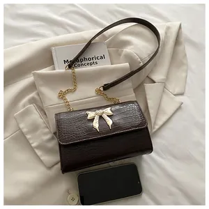 Detail of crocodile pattern texture on dark brown bag with golden bow clasp and chain strap