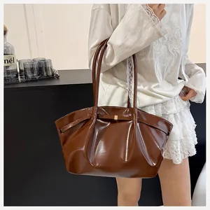 Détail du sac seau marron en cuir verni avec sangle décorative et boucle dorée chic