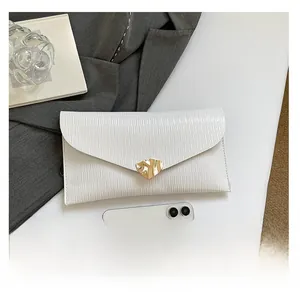 Détail de la pochette plissée blanche avec boucle dorée à côté d'un smartphone pour taille