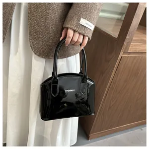 Close-up of black patent leather shell bag with silver FASHION logo and top handle