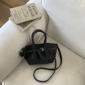 Top view of a black woven bucket bag on a white sofa next to vintage books