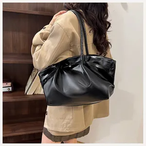 Grand sac fourre-tout en cuir verni noir avec de longues bandoulières sur un modèle