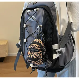 Close-up of leopard print mini bag charm attached to a grey outdoor shoulder bag