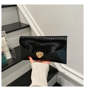 Détail de la pochette enveloppe noire vernie avec boucle feuille dorée et texture ondulée