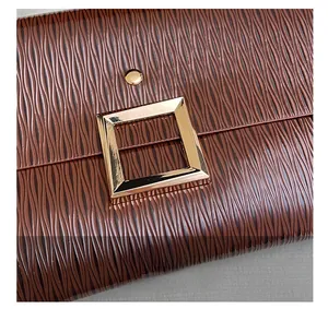 Gros plan sur la texture ondulée marron et la boucle carrée en métal doré de ce sac à main