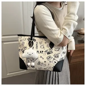 Detail of a large cream tote bag with graffiti prints and a plush cloud charm accessory