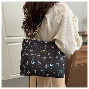 Detail of black tote bag featuring colorful butterfly embroidery and gold chain strap