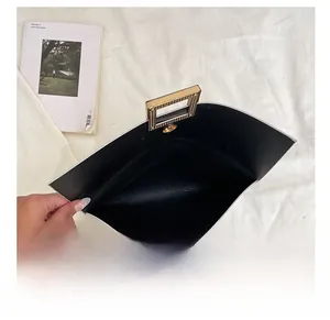 Vue de dessus d'une pochette noire en PU avec poignée dorée et intérieur spacieux
