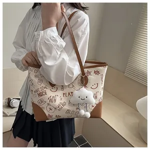 Detail of cream tote bag with cartoon graffiti, brown handles, and cloud plush charm