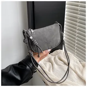 Nahaufnahme der grauen Wildledertasche mit Knotengurt und silbernem M-Anhänger