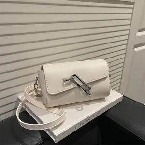 Minimalistische beige Umhängetasche mit silbernem Schloss auf einem Dekobuch