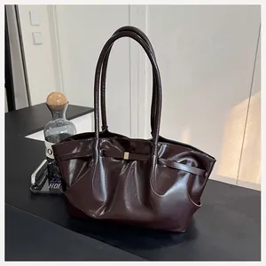 Détail d'un sac seau en cuir marron foncé brillant avec boucle dorée et design plissé