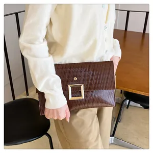 Détail montrant les plis verticaux et la boucle dorée carrée sur une pochette marron foncé
