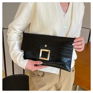 Détail d'une pochette en cuir verni noir avec une grande boucle carrée en métal doré