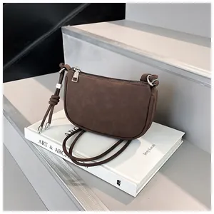 Detail einer braunen Wildleder-Hobo-Tasche mit Knotendesign auf einem Buch-Requisit