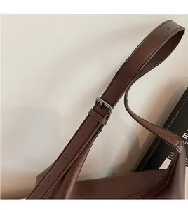 Dettaglio della tracolla regolabile su una borsa tote in pelle marrone morbida opaca