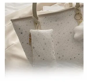 Close-up of a white star pattern coin purse charm on a tote bag with gold zipper detail