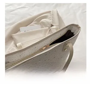 Detailed view of gold metal zipper and star print on cream tote bag with dark lining
