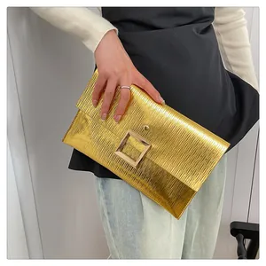 Détail d'une pochette enveloppe dorée métallisée avec texture ondulée et boucle carrée