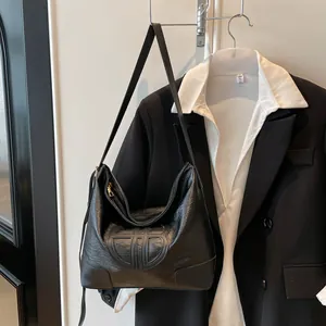 Détail du cabas noir en cuir grainé avec logo embossé sur fond de blazer noir élégant