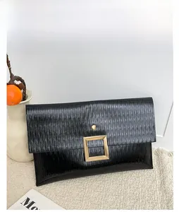 Détail d'une pochette noire à rabat avec plis verticaux et boucle dorée sur un tapis